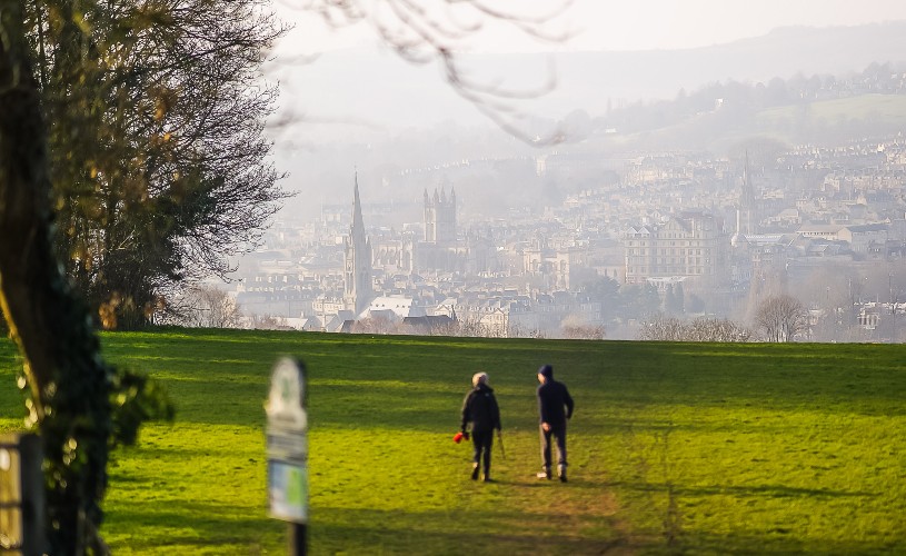 Two people walking across field with Bath skyline in the background